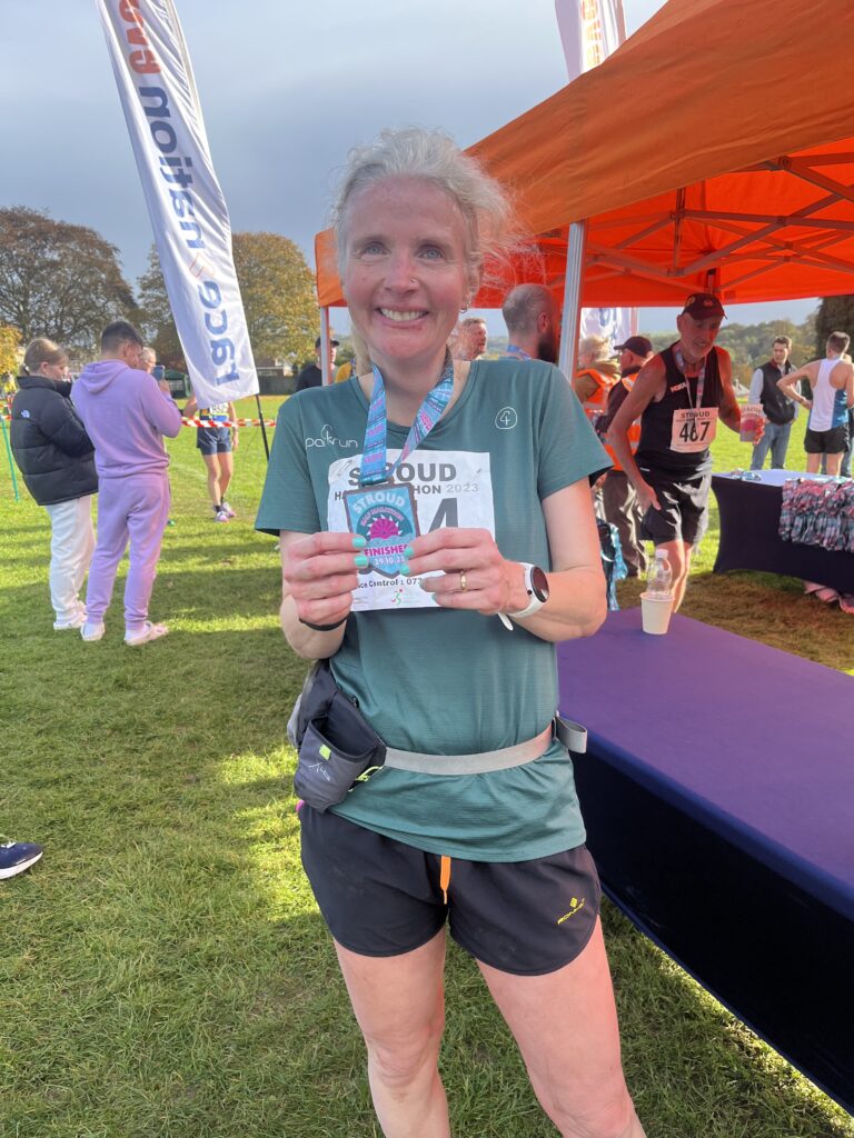 Stroud half marathon, Stroud half marathon medal, Medal, Running, Runner, Female runner in a green top holds a blue and pink wooden medal