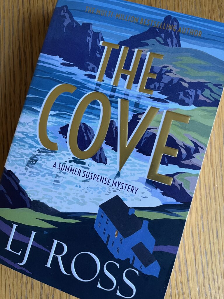 The Cove by LJ Ross, The Cove, LJ Ross, Book review, A book entitled The Cove by LJ Ross with a picture of rocks and the sea sits on a wooden table