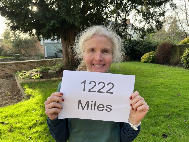 Running, Mileage, Distance, Runner, How far did I run in 2023, Head and shoulders photo of a smiling woman in a garden holding a piece of paper which reads 1222 miles