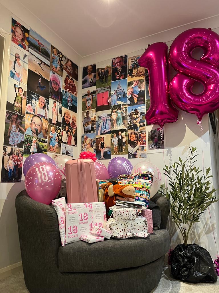 18th birthday, Birthday presents, Balloons, A pile of birthday presents sit on a grey chair with a large pair of pink balloons making up the number 18 and lots of photos of a young girl in the background