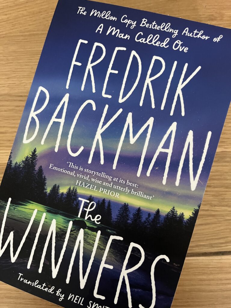 The Winners by Fredrik Backman, The Winners, Fredrik Backman, Book review, A blue book called The Winners by Fredrik Backman sits on a wooden table