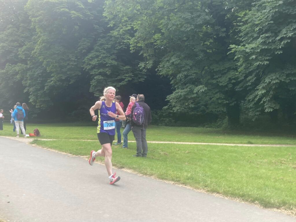 Running, Runner, Cirencester 10k, A female runner in a purple vest and black shorts grimaces as she runs through a park