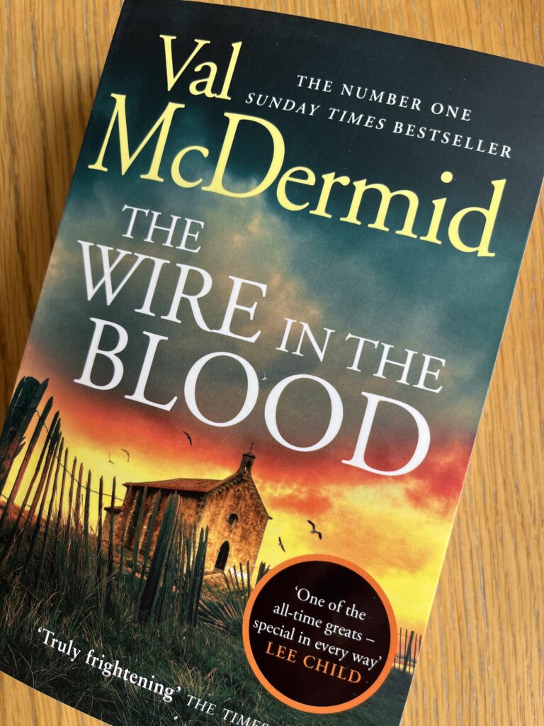 The Wire in the Blood by Val McDermid, The Wire in the Blood, Val McDermid, Book review, A book called The Wire in the Blood by Val McDermid with a dramatic sky on the cover sits on a wooden table