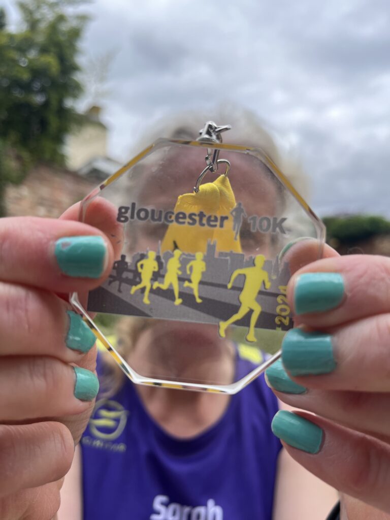 Gloucester 10k, Gloucester 10k medal, Running, Runner, Silent Sunday, My Sunday Photo, Close-up of a clear medal with yellow runners on it which says Gloucester 10k held by a woman with blue nail varnish