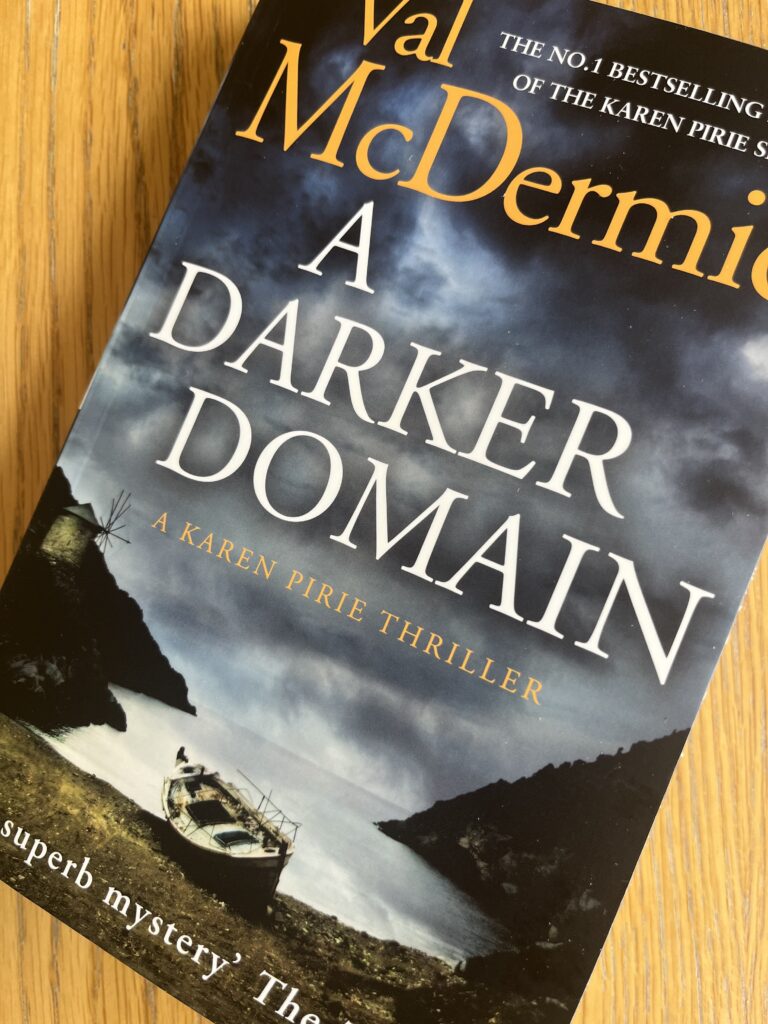 A Darker Domain by Val McDermid, A Darker Domain, Val McDermid, A book with a dark cover called A Darker Domain by Val McDermid sits on a wooden table