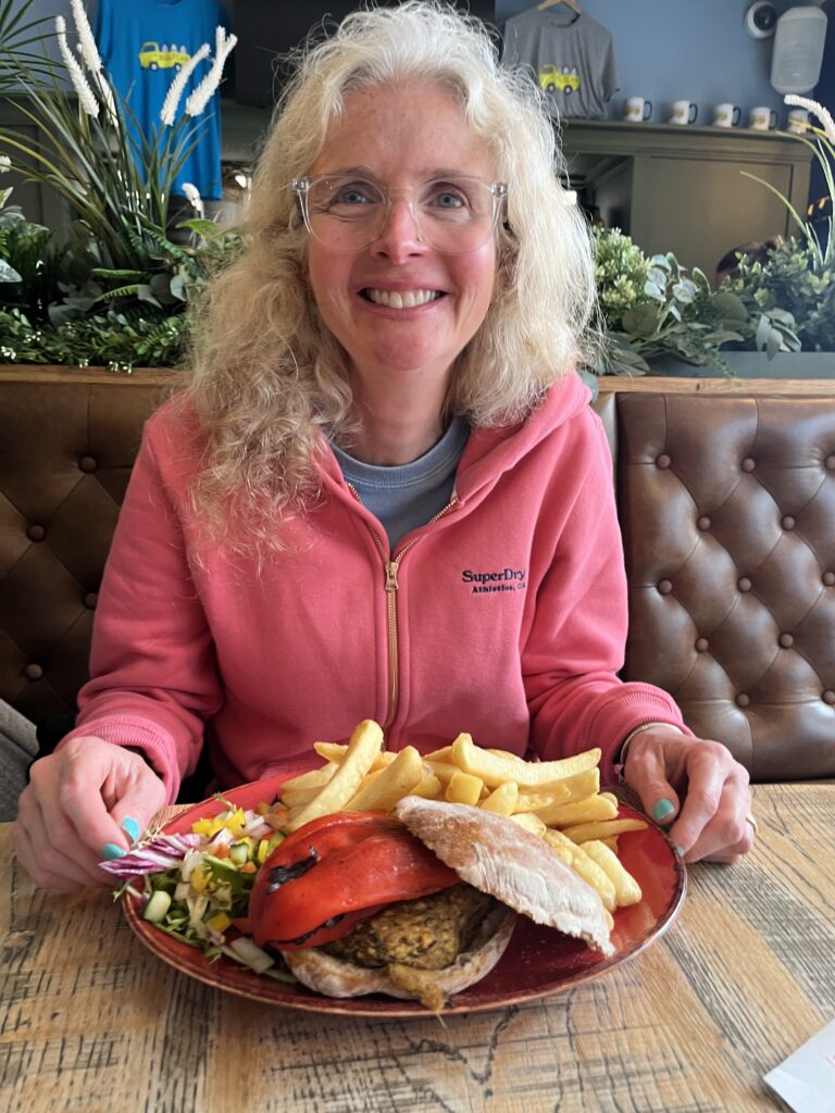 Burger, Vegan burger, A smiling woman in a pink hoodies holds a plate with a large burger and chips