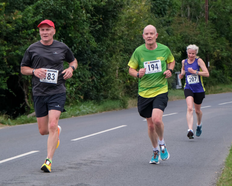 Runners, Running, Race, Bugatti 10k, Two older male runners and a female runner in a purple vest run along a road