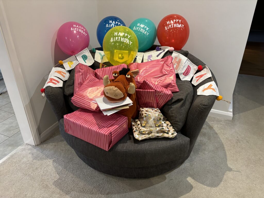 Birthday, 51st birthday, Balloons, Birthday presents, Pumbaa, Silent Sunday, My Sunday Photo, A pile of birthday presents sits on a round grey armchair with a toy Pumbaa from The Lion King in the middle and colourful birthday balloons