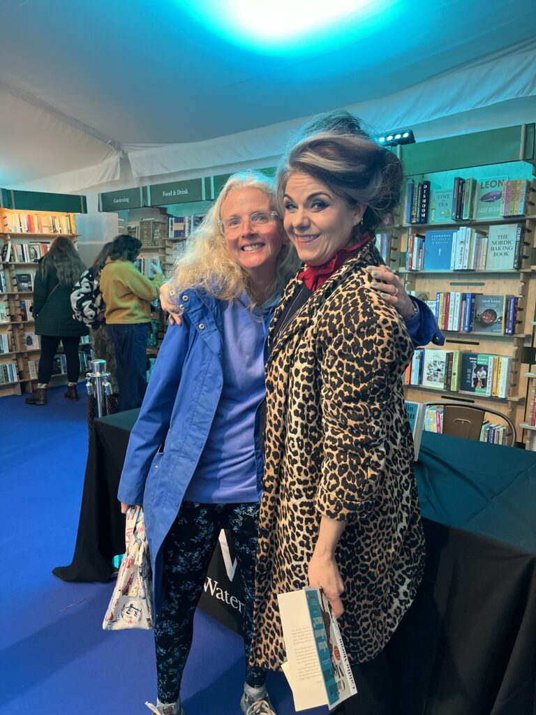 Caitlin Moran, Cheltenham Literature Festival, Silent Sunday, My Sunday Photo, Two middle aged women hug one of them has big dark hair with a grey streak and is wearing a leopard skin coat and the other one has blonde hair and glasses and is dressed in blue