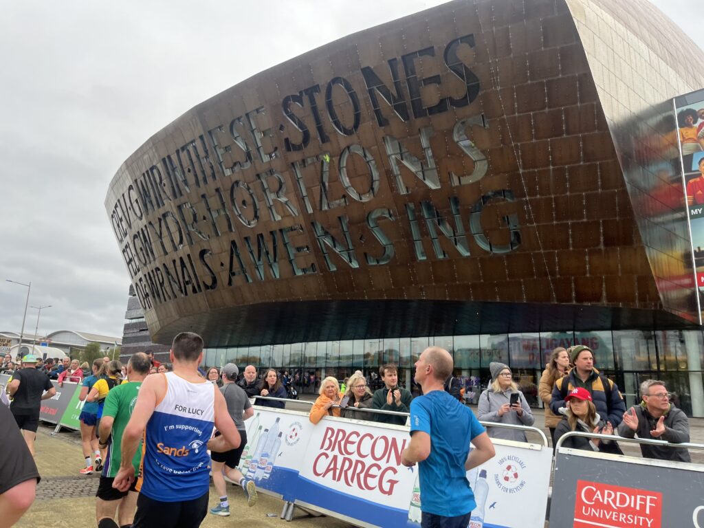 Cardiff half marathon, Millennium Centre, Runners, Runners run past a large bronze building which is the Millennium Centre in Cardiff while spectators watch