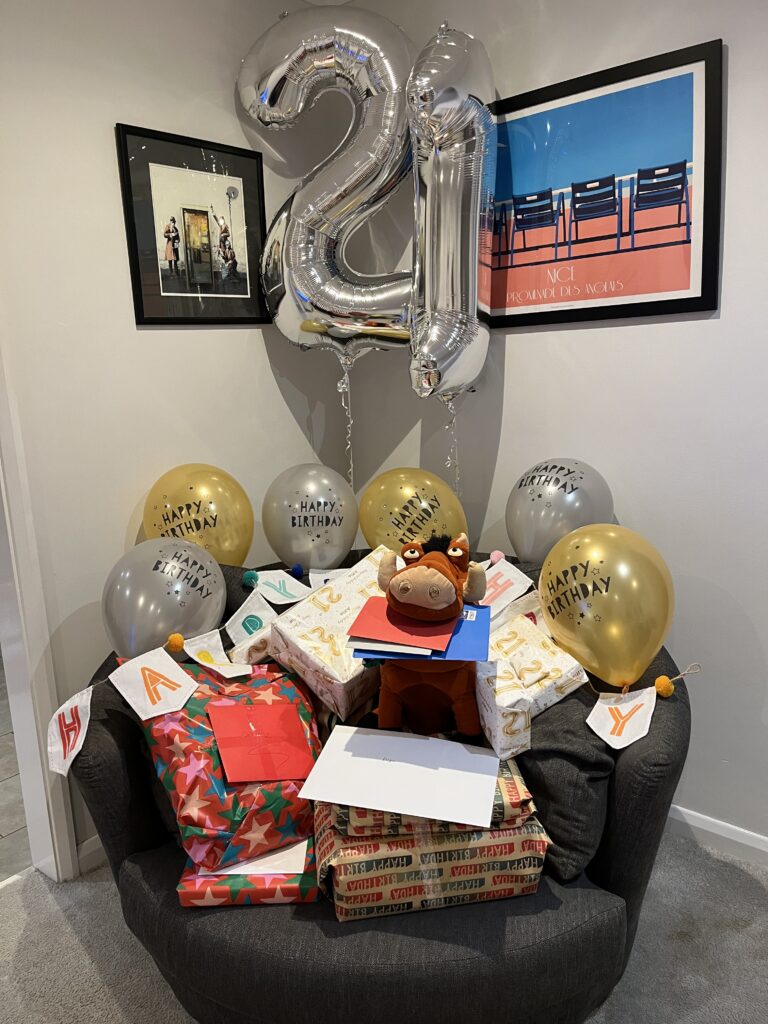 Birthday, 21st birthday, Birthday presents, Son, Silent Sunday, My Sunday Photo, Pumbaa, A pile of birthday presents sit on a round grey armchair with a brown cuddly toy in the middle of them and surrounded by gold and silver happy birthday balloons with two big silver balloons behind them - a number 2 and a number 1