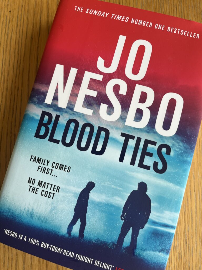Blood Ties by Jo Nesbo, Blood Ties, Jo Nesbo, Book review, A red and blue book with two silhouetted figures on the cover called Blood Ties by Jo Nesbo sits on a wooden table