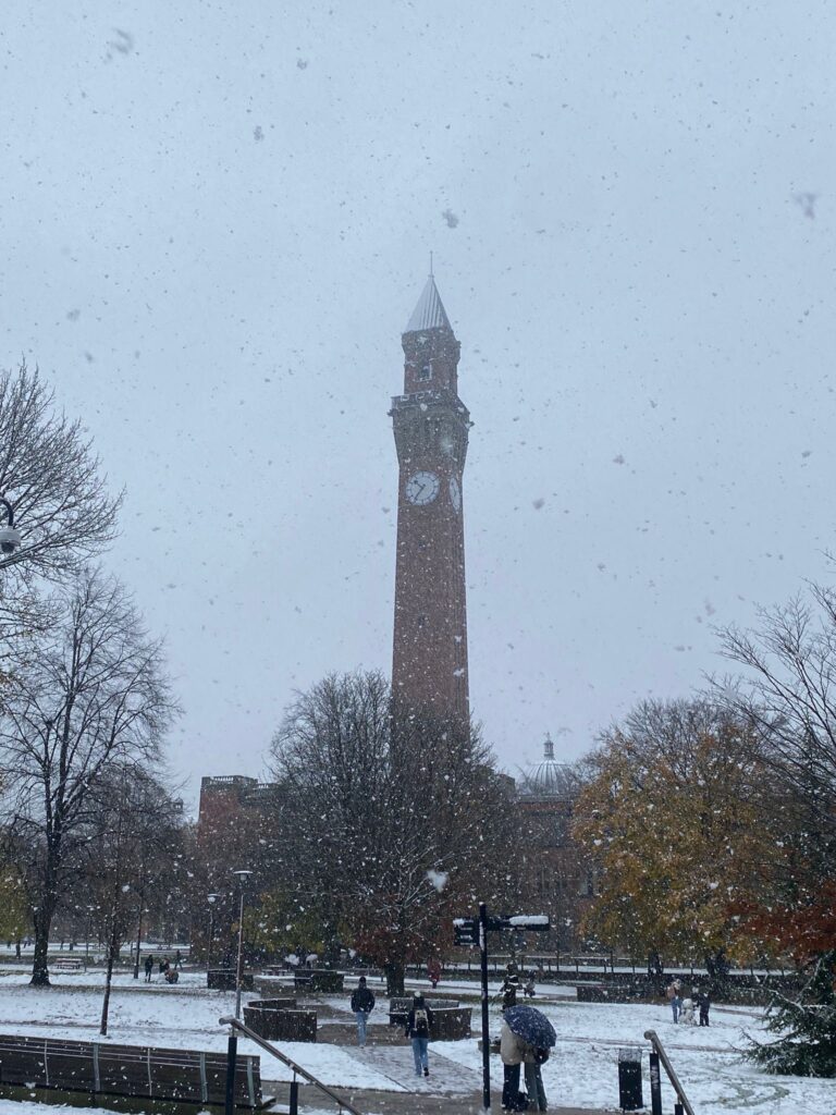 University of Birmingham, Birmingham University, Old Joe, Snow, Silent Sunday, My Sunday Photo, A very tall clock tower surrounded by bare trees with a few few people walking while snow is falling and there is snow on the ground and the sky is grey