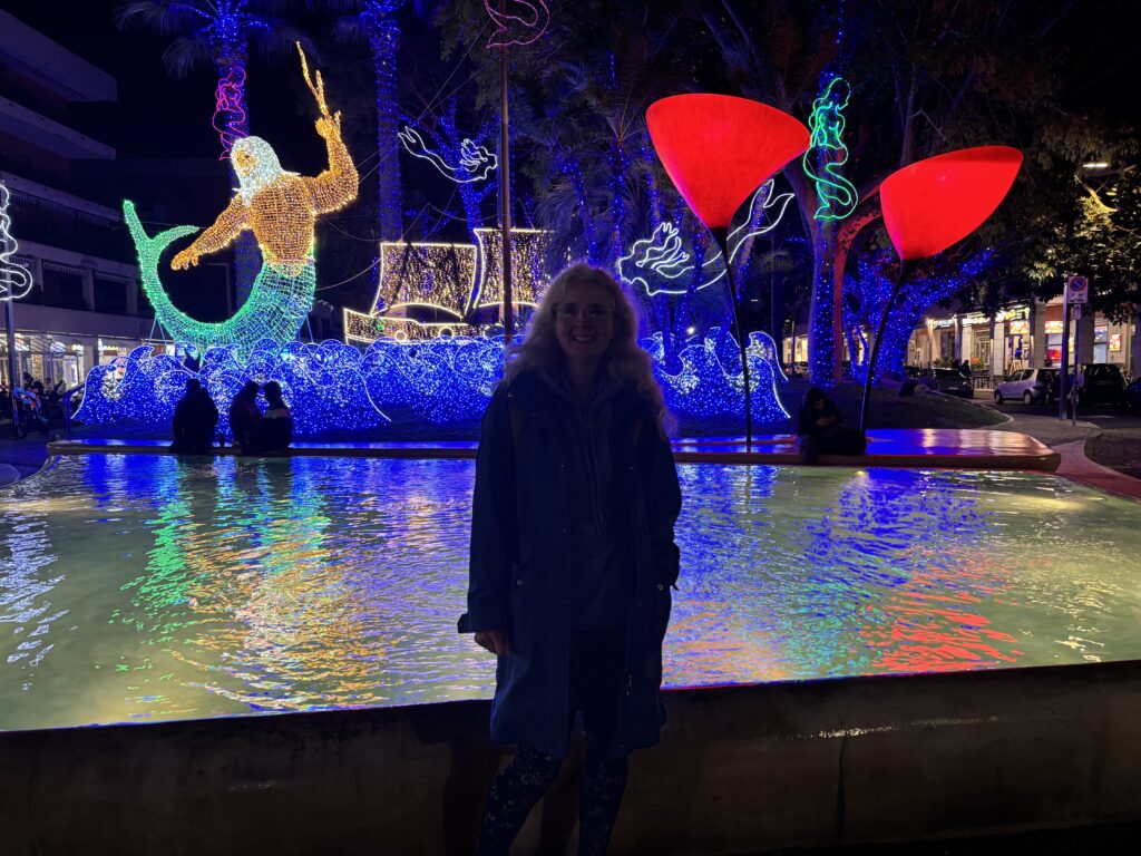 Sorrento, Italy, Neptune in lights, A silhouetted woman in darkness stands in front of a large Neptune and boat and waves made from coloured lights