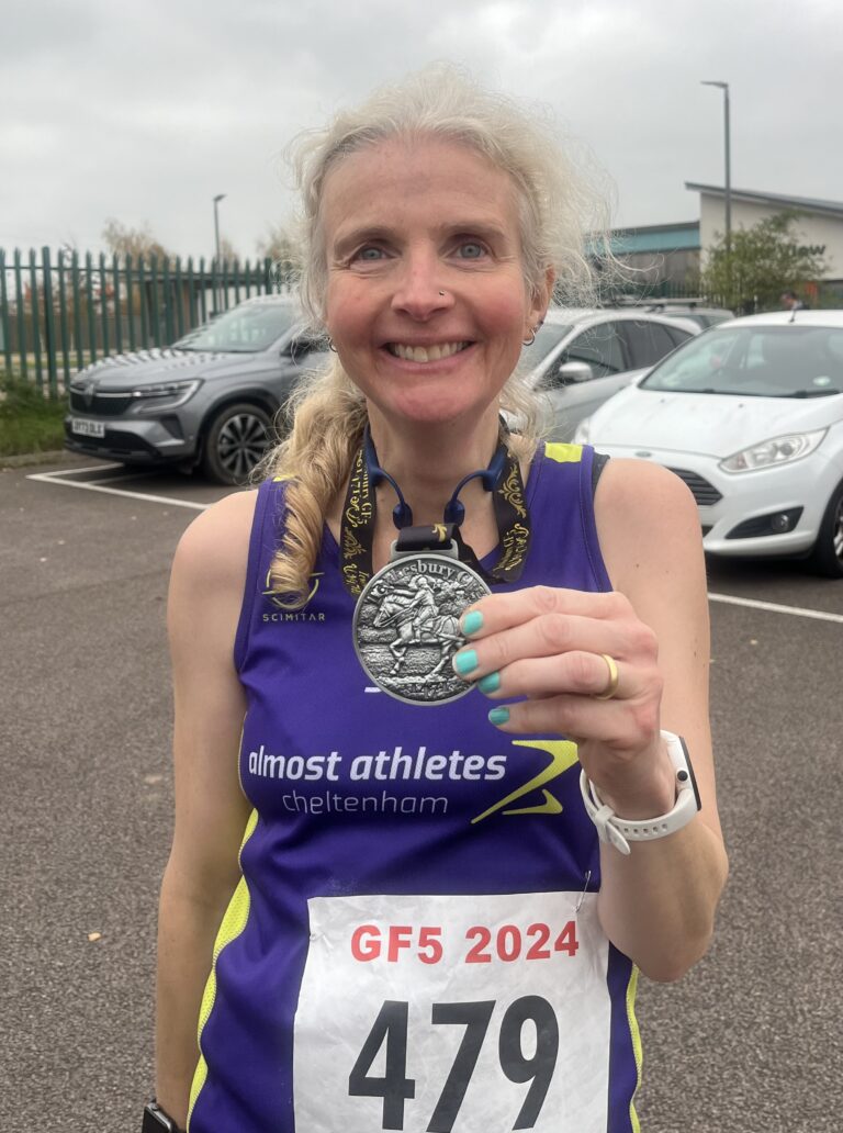 Guy Fawkes 5, Guy Fawkes 5 medal, Running, Runner, A smiling female runner in a purple vest holds up a metal medal