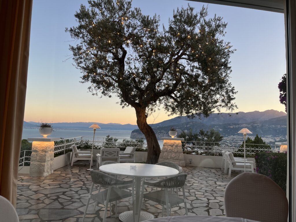 Sorrento, Grand Hotel Aminta, Italy, HOtel terrace, A paved terrace with tables and chairs and an olive tree overlooks mountains and the sea