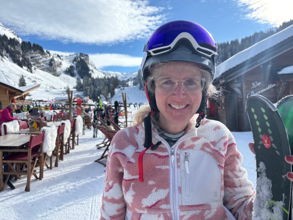 Skiing holiday, Alps, Les Lindarets, France, A smiling woman stands in the snowy mountain with a ski helmet and blue goggles on her head and wearing a pink and white fleece