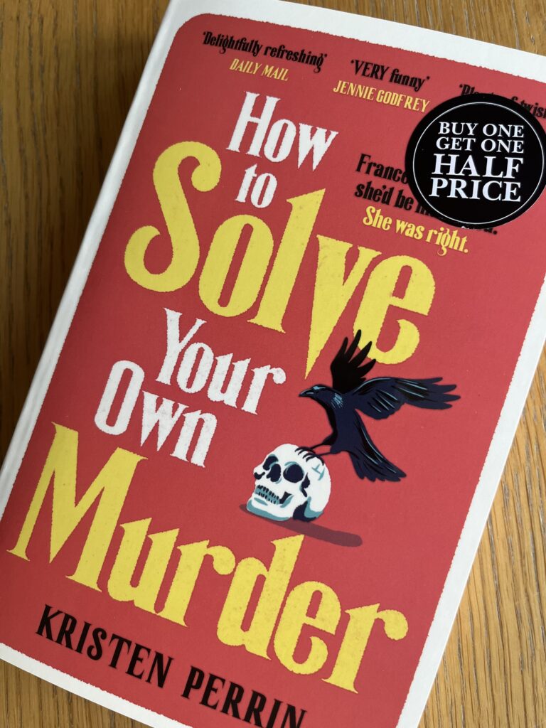 How to Solve Your Own Murder by Kristen Perrin, How to Solve Your Own Murder, Kristen Perrin, Book review, A red book with red and yellow writing and the image of a skull and a black bird called How to Solve Your Own Murder by Kristen Perrin sits on a wooden table