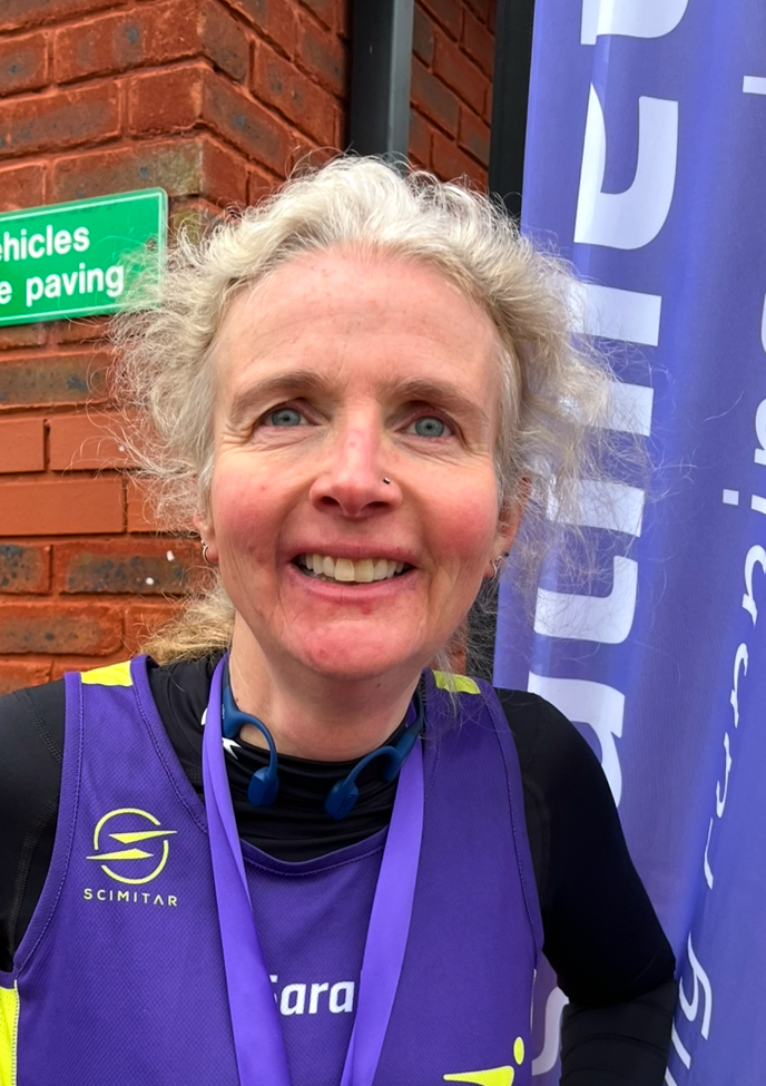 Linda Franks Race, Linda Franks Race medal, Head and shoulders photo of a smiling female runner in a purple vest over a black top with the purple ribbon of a medal around her neck