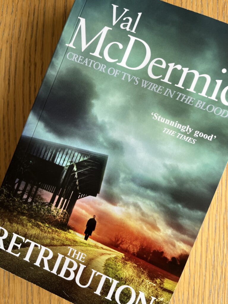 The Retribution by Val McDermid, The Retribution, Val McDermid, Book review, A book called The Retribution by Val McDermid with a stormy sky and the silhouette of a man and a building on the cover sits on a wooden table
