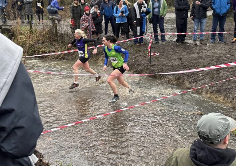 Cross country, Cross country race, Running, Runners, Silent Sunday, My Sunday Photo, Two female runners run through a stream with red and white tape on either side and a crowd of people watching