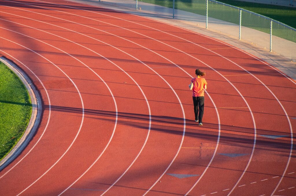 Running track, Runner, Athlete, A woman in an orange top and black trousers runs round a track