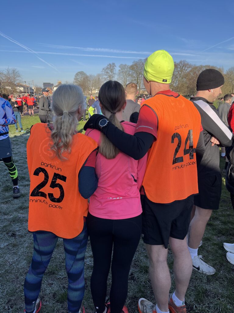 Parkrun, Husband, Daughter, Volunteering, Rear view of two female and one male runners and the two runners on the outside are wearing orange vests with large numbers on the back
