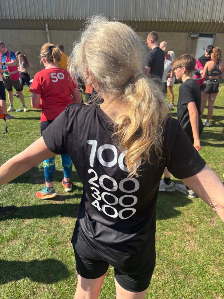 Parkrun, 400th parkrun, The back of a woman with long hair wearing a black shorts and a black Tshirt with the numbers 100 200 300 and 400 on it in white print