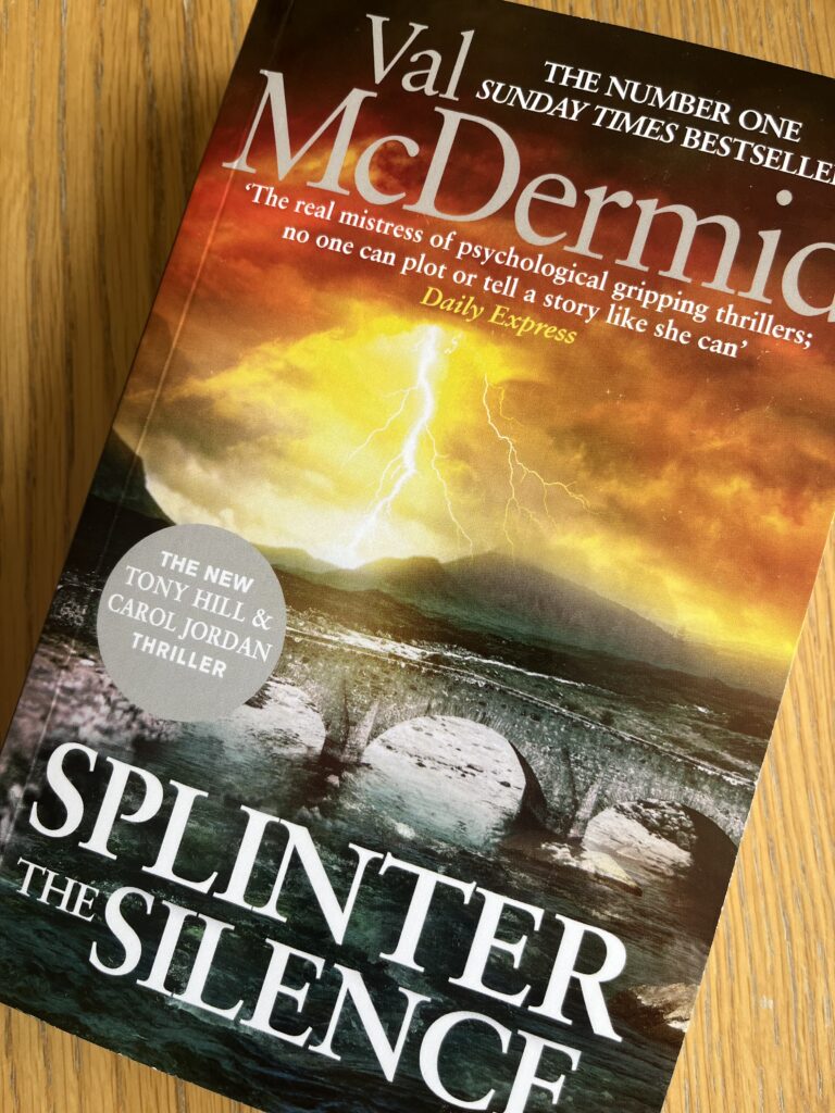 Splinter the Silence by Val McDermid, Splinter the Silence, Val McDermid, Book review, A book called Splinter the Silence by Val McDermid with an orange sky and a fork of lightning over an old stone bridge sits on a wooden table