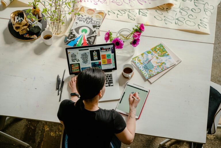 Remote work, Work from home, View from above of a woman sitting at a large desk working on a laptop and drawing on a tablet
