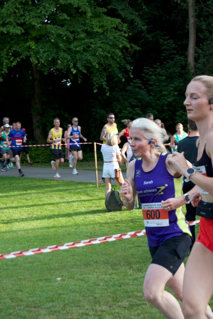 Cirencester Summer Sizzler, Cirencester 10k, Runners, Running, A female runner in a purple vest tries to overtake a younger and taller female runner with a stream of other runners in the background
