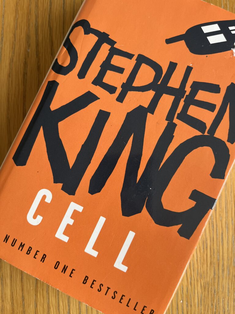 Cell by Stephen King, Cell, Stephen King, Book review, An orange book with a drawing of a mobile phone on the front called Cell by Stephen King sits on a wooden table
