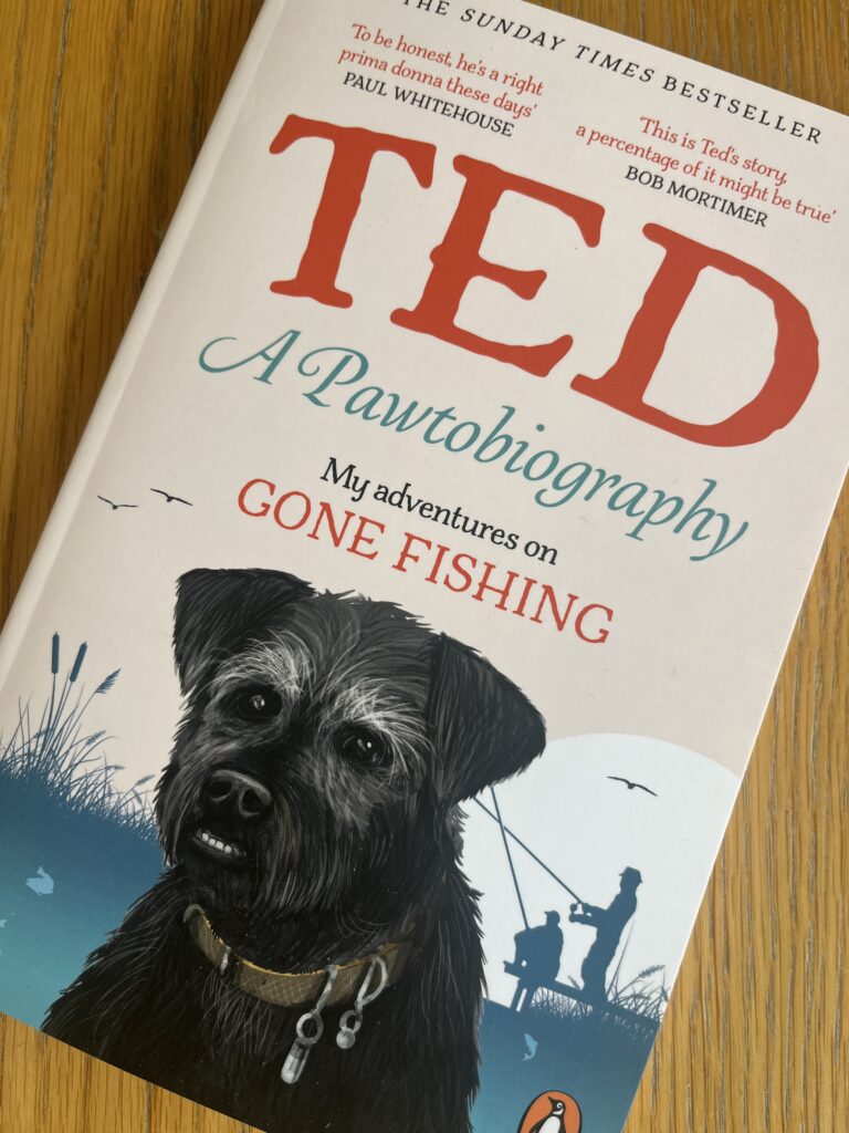 Ted A Pawtobiography, Ted A Pawtobiography review, Book review, Gone Fishing, A cream coloured book with red writing and a black dog with prominent teeth on the cover called Ted A Pawtobiography sits on a wooden table