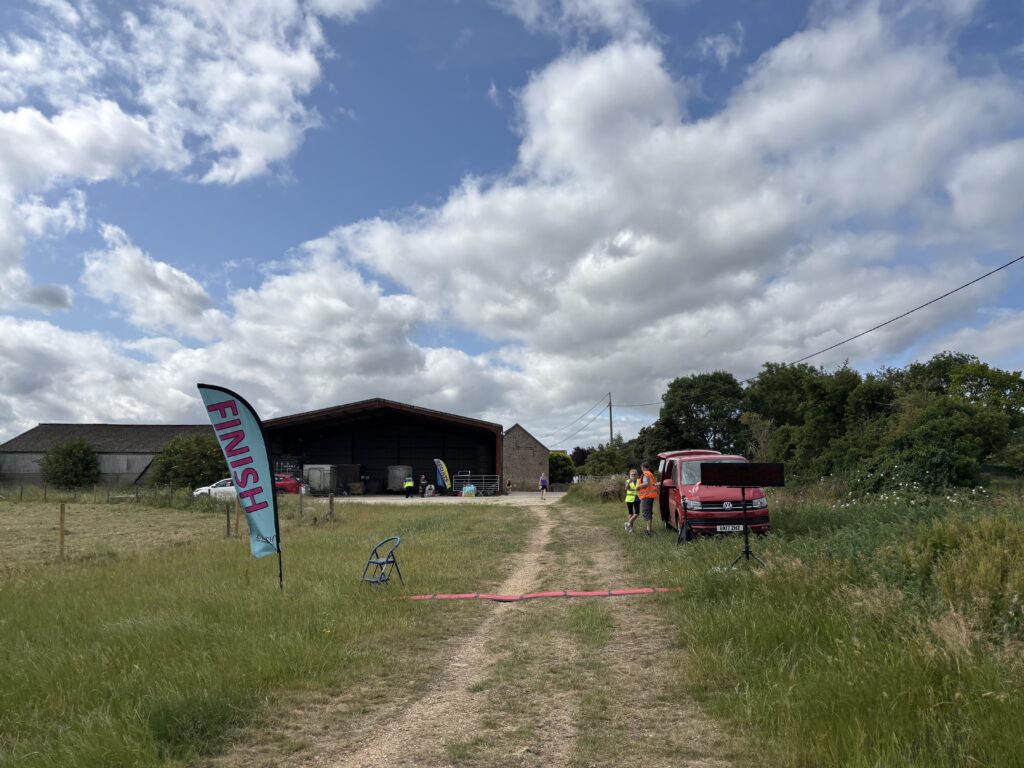 Greystones 10k, Finish line, A field and a blue sky with farm buildings in the background and a blue flag which says finish and a red van