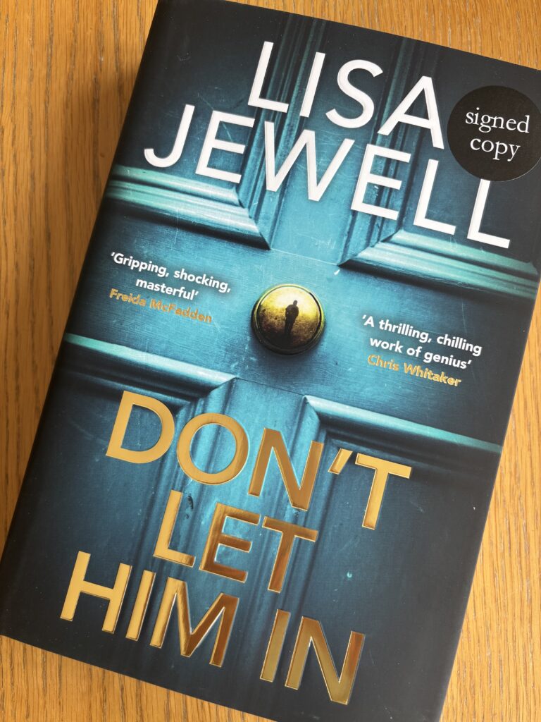 Don't Let Him In by Lisa Jewell, Don't Let Him In, Lisa Jewell, Book review, A blue book showing a close up of a door with a man reflected on a gold doorknob called Don't Let Him In by Lisa Jewell sits on a wooden table