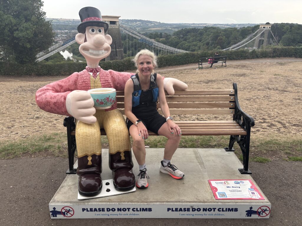 Gromit Unleashed 3, Wallace and Gromit, Clifton Suspension Bridge, Bristol, Silent Sunday, My Sunday Photo, A female runner in a black vest and shorts sits on a bench next to a large coloured Wallace sculpture with a suspension bridge in the background