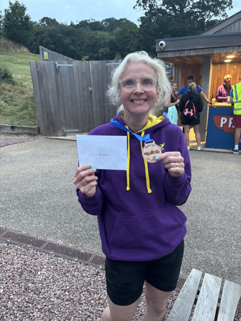 Bugatti 10k, Prize winner, Runner, A smiling woman in a purple jumper holds a wooden medal and an envelope