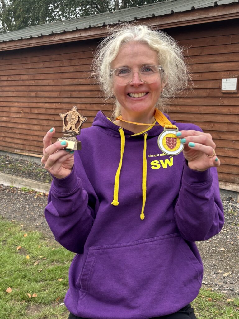 Angels 10k, Running, Runner, A smiling female runner in a purple hoodie holds up a medal and a small trophy