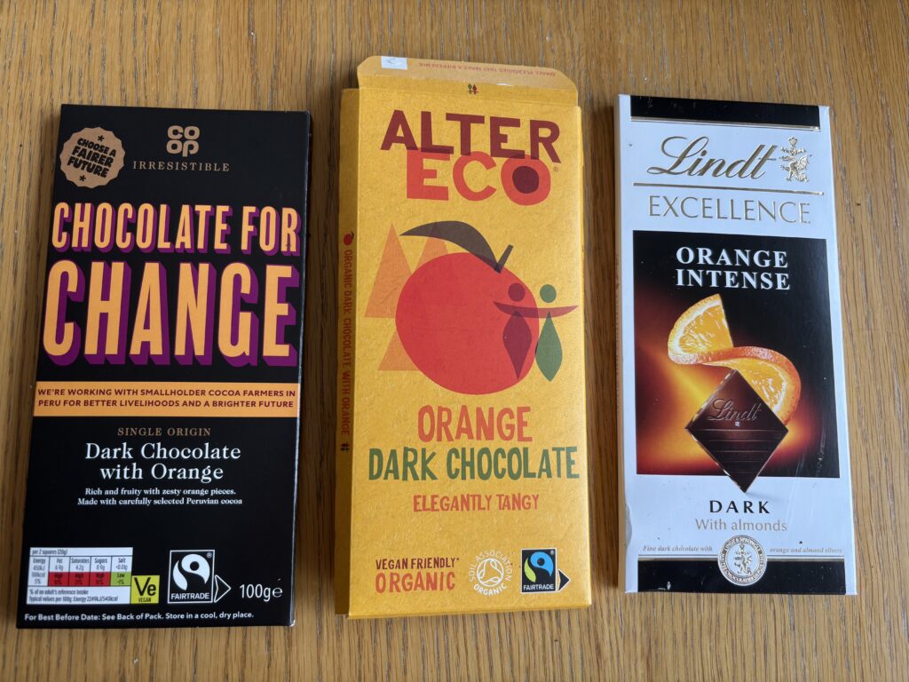 Three different wrapped bars of orange flavoured dark chocolate sit on a wooden table