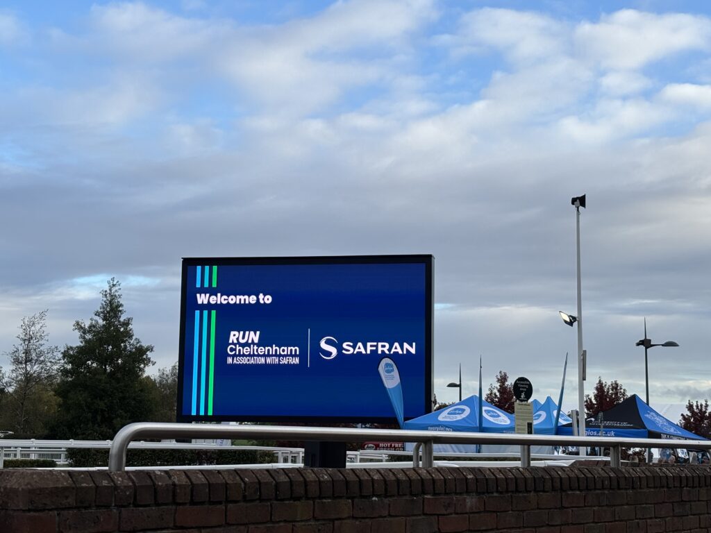 Run Cheltenham, Cheltenham half marathon, Cheltenham racecourse, A big screen says Welcome to Run Cheltenham against a cloudy sky