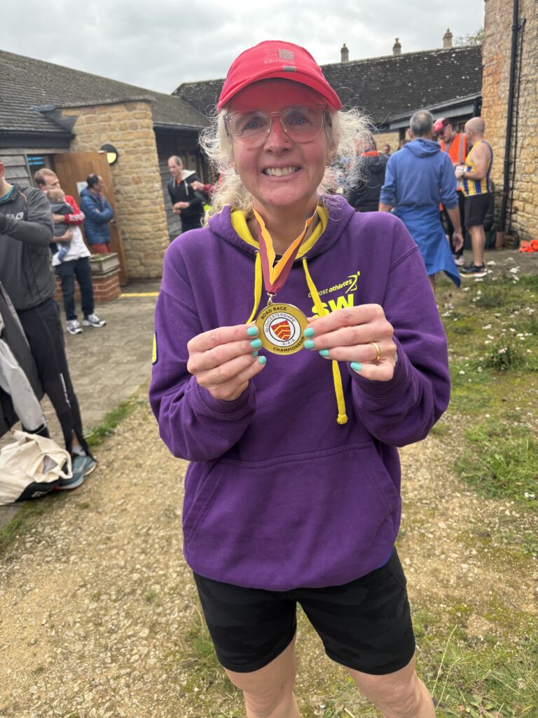 Bourton half marathon, Bourton hilly half, Half marathon county champion, Running, Runner, A woman in a purple hoodie and pink hat wearing a medal which says Road Race Championship