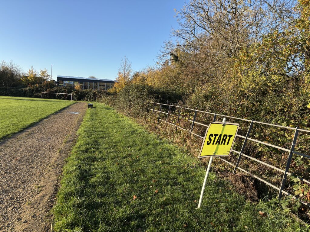 Kingsway parkrun, Parkrun, Parkrun tourism, A yellow start sign in the grass next to a straight path and some grass and lots of trees with brown leaves