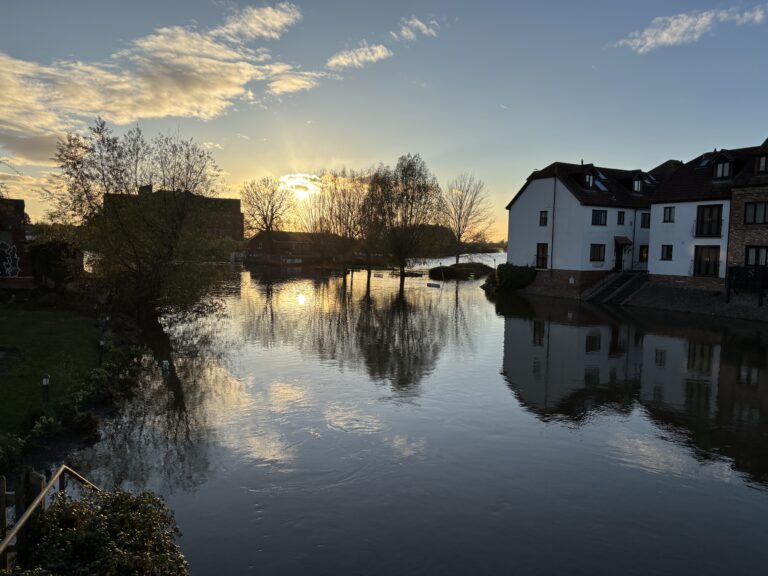 Tewkesbury, Gloucestershire, Floods, Reflections, Silent Sunday, My Sunday Photo, A vast expanse of water with a white building and several trees reflected in it at dusk with the sun low in the sky
