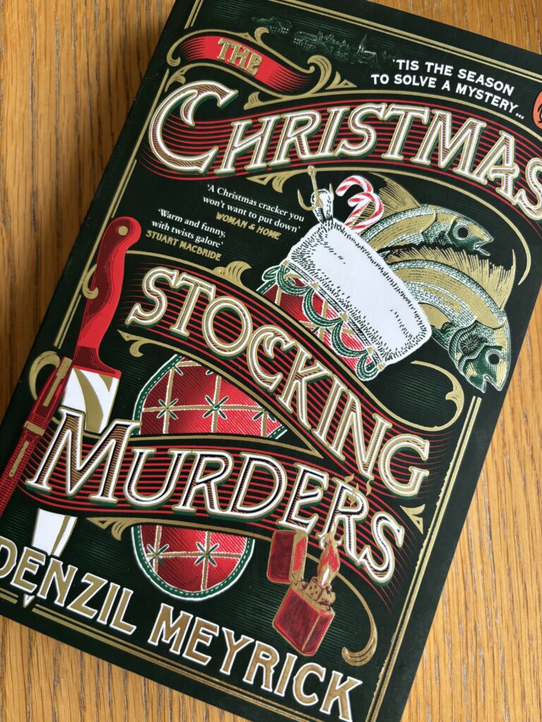 The Christmas Stocking Murders by Denzil Meyrick, The Christmas Stocking Murders, Denzil Meyrick, Book review, A dark green book with a red Christmas stocking on the front called The Christmas Stocking Murders by Denzil Meyrick sits on a wooden table