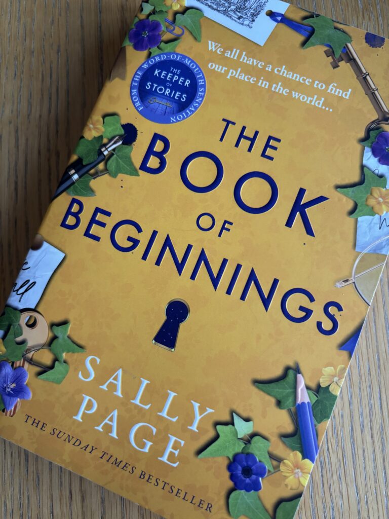 The Book of Beginnings by Sally Page, The Book of Beginnings, Sally Page, Book review, A yellow book with ivy leaves and purple and yellow flowers round the edges called The Book of Beginnings by Sally Page sits on a wooden table