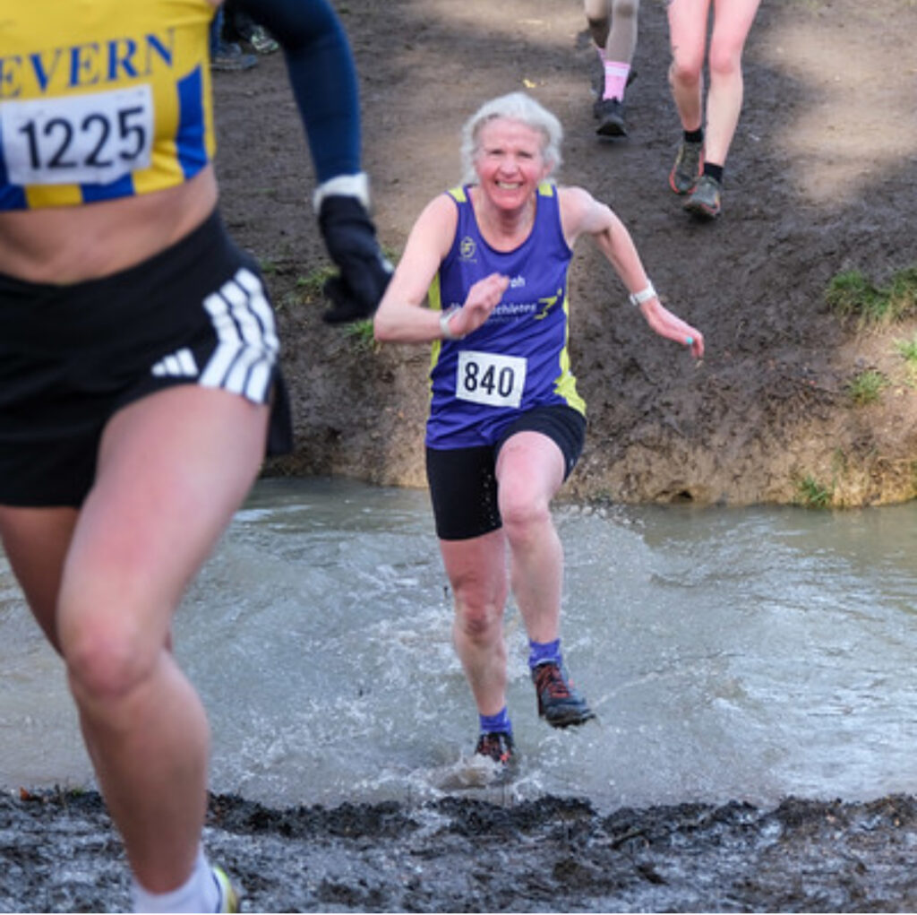 Cross country, Pittville Park cross country, Running, Runner, A female runner in purple vest and black shorts grimaces as she runs through a stream