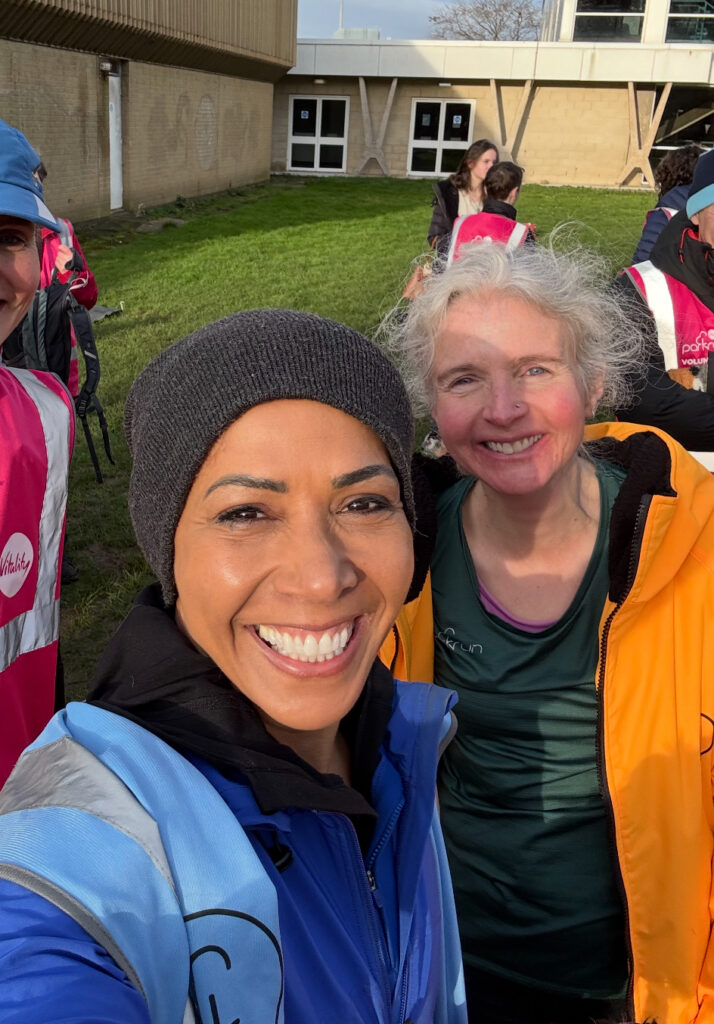 Dame Kelly Holmes, Parkrun, Silent Sunday, My Sunday Photo, Selfie of a smiling black woman in a black hat and blue clothing in front of a smiling with woman in a big apricot coloured coat