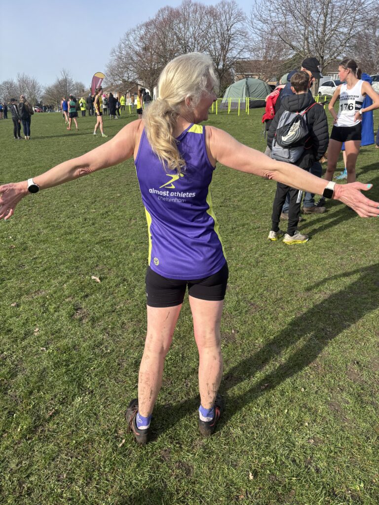 Cross country, Pittville Park cross country, Running, Runner, A female runner in black shorts and a purple vest stands on the grass with her back to the camera showing all the mud on her legs
