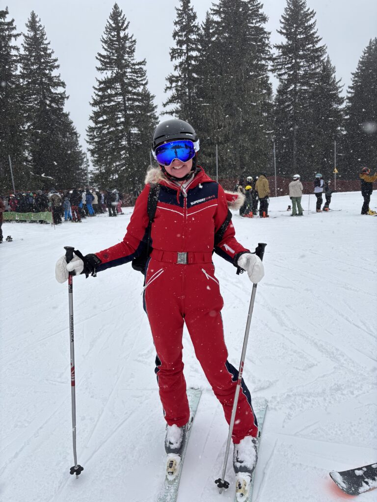 Snow, Skiing, Avoriaz, Alps, A female skier in a red suit and blue goggles stands in the falling snow with tall trees in the background