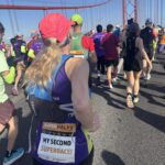 Lisbon half marathon, Runners, Running, Pont de 25 Abril, Lisbon, Silent Sunday, My Sunday Photo, A crowd of runners run across a big red bridge against a blue sky with a female runner in a pink hat and a sign on her back saying My Second Superrace in the foreground
